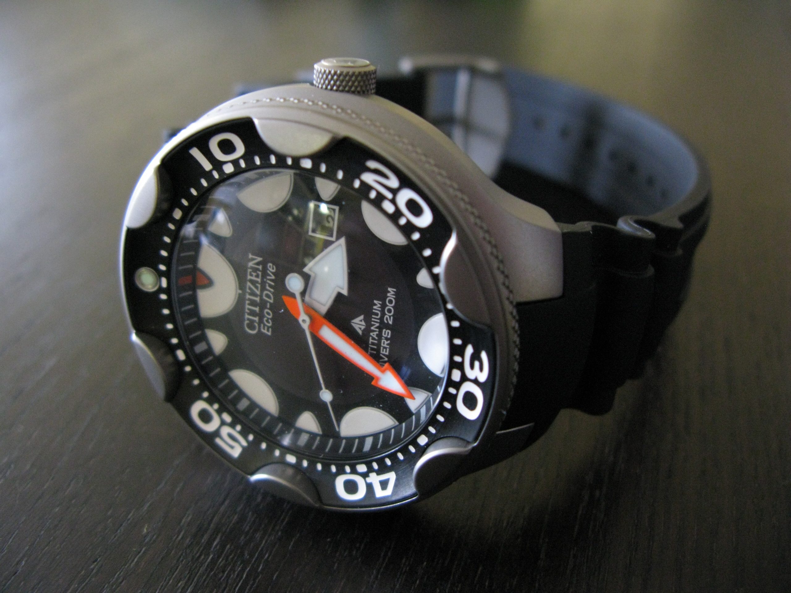 Relógio de mergulho Citizen Eco-Drive de caixa de titânio sobre uma mesa escura, com luneta giratória preta numerada, ponteiro laranja e a inscrição Titanium Diver's 200m no mostrador.